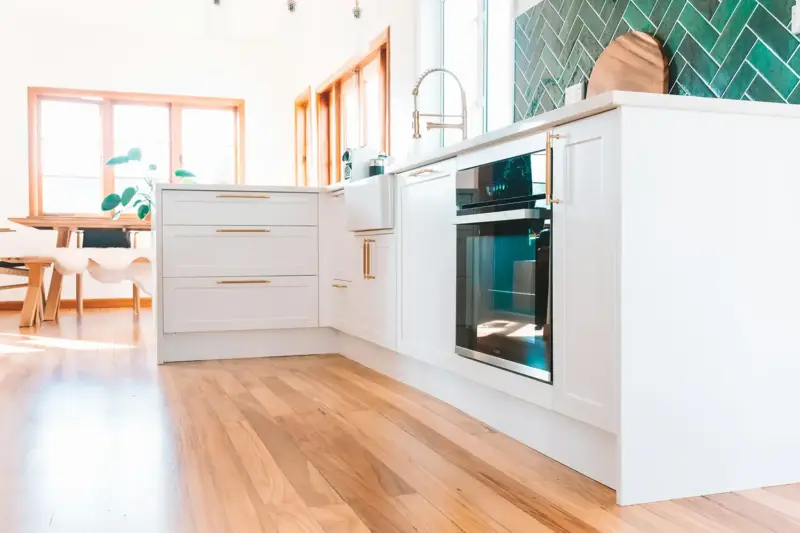 Custom white kitchen cabinetry with brass handles and green tile splashback, Whangārei